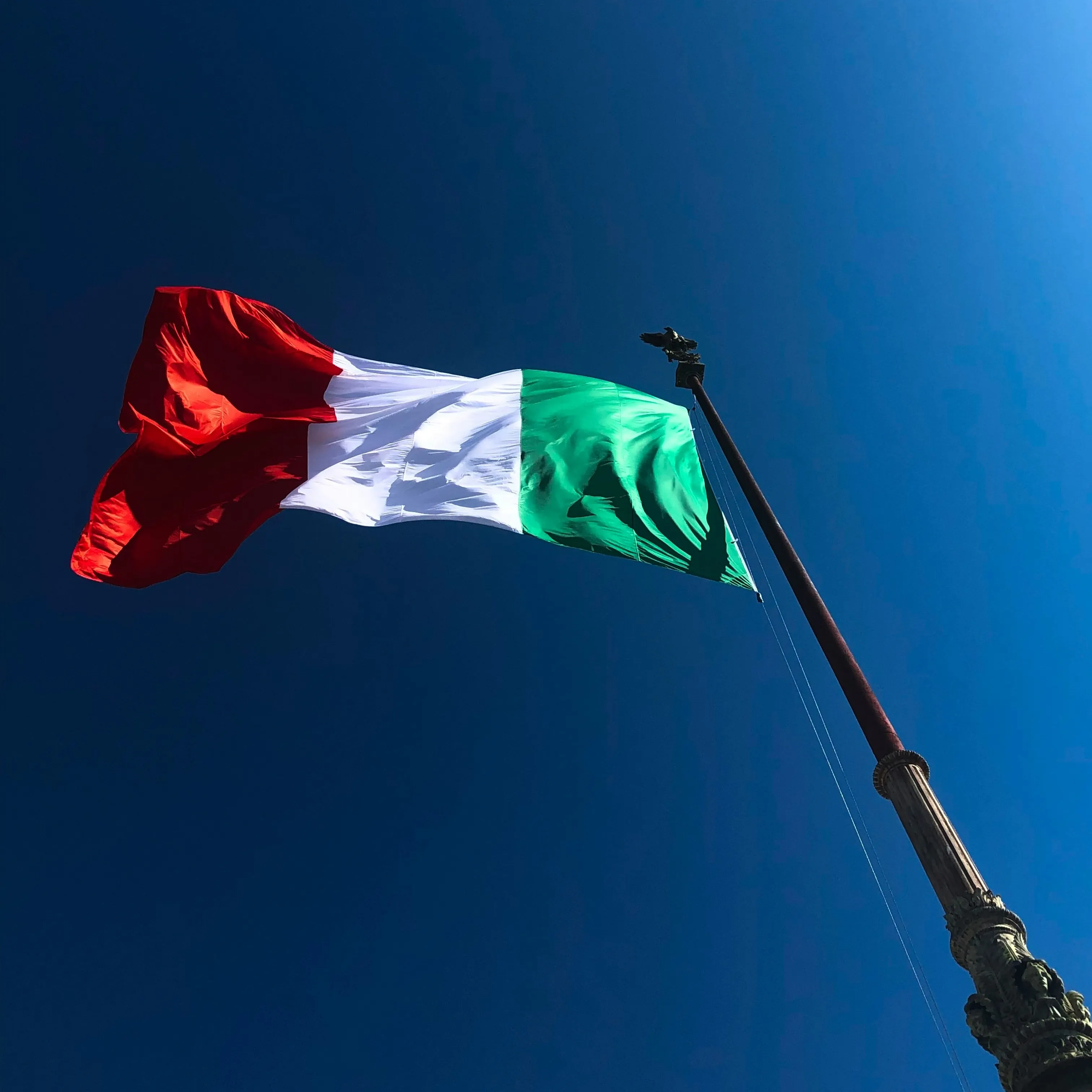 Italienische Flagge weht an einem Mast vor blauem Himmel.
